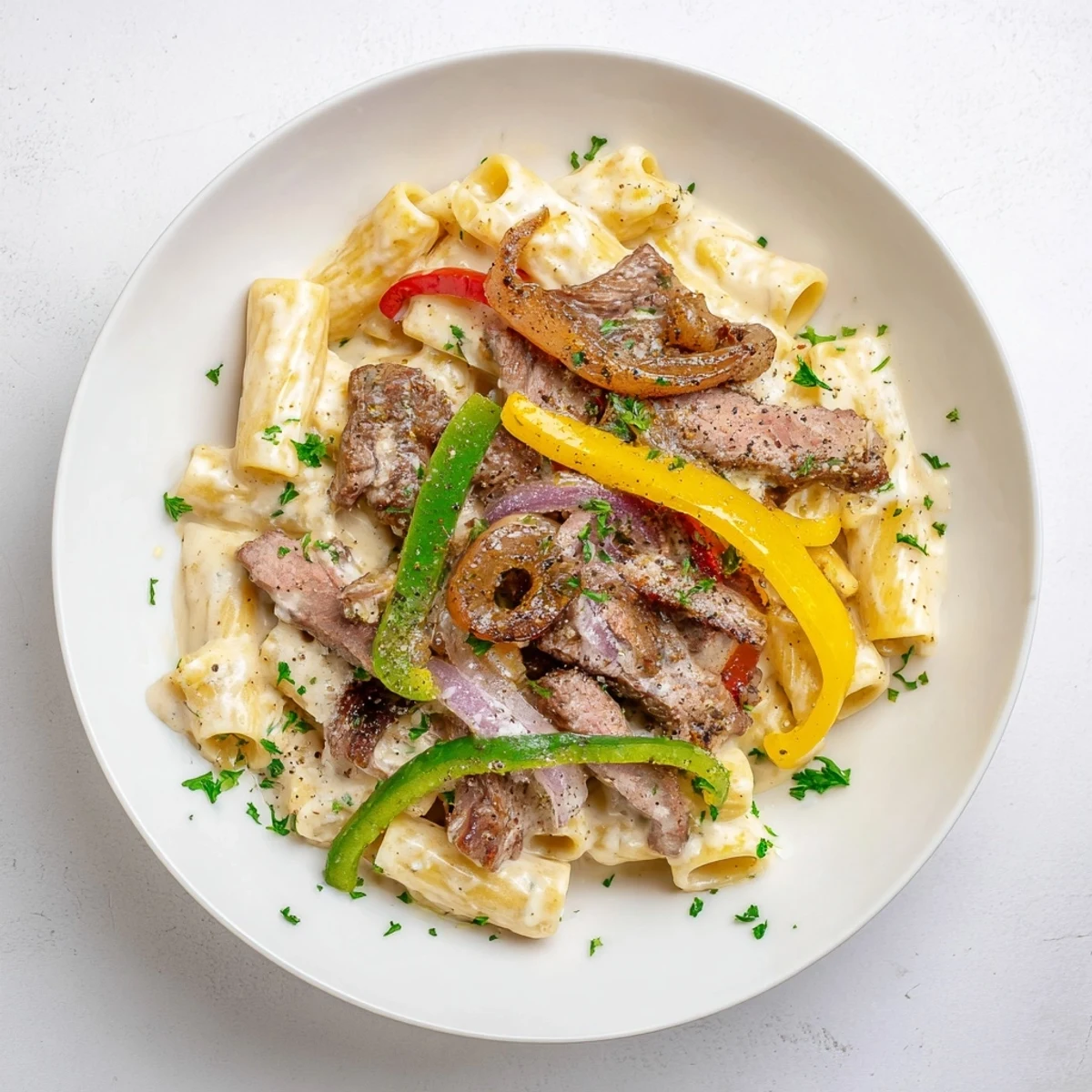 A steaming bowl of Philly Cheese Steak Pasta, garnished with fresh parsley and smelling delicious.