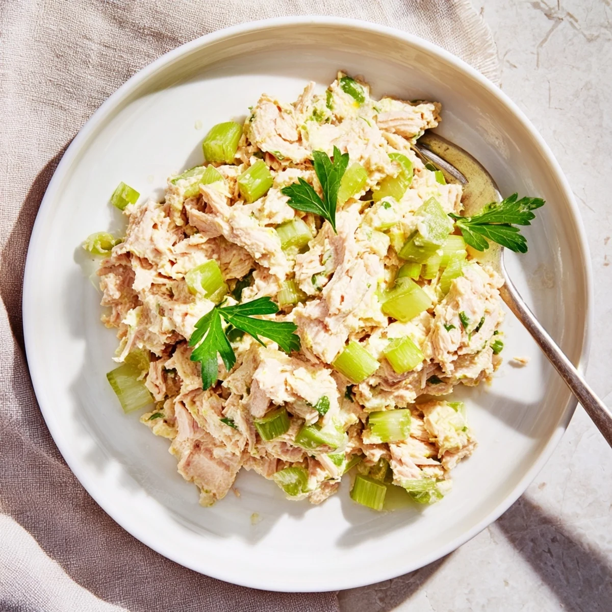 Freshly mixed Spicy Zesty Tuna Salad with creamy orange dressing, scallions, and lemon wedges on a rustic plate.