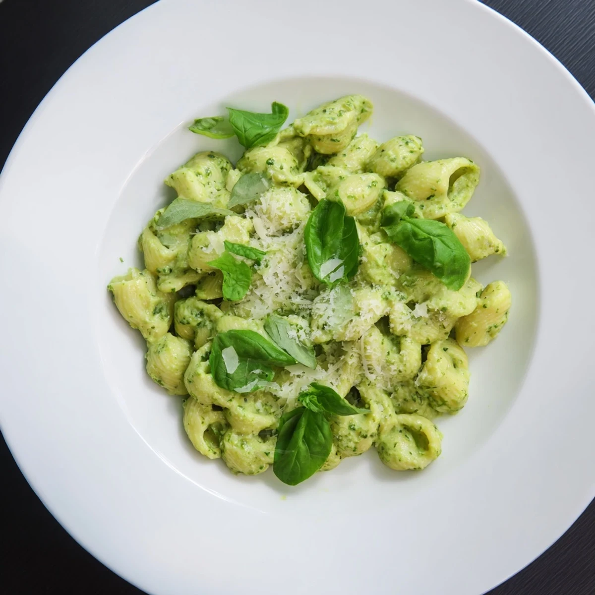 Freshly tossed Creamy Avocado Pesto Mac in a white bowl, garnished with basil and parmesan, served warm as a vibrant green main dish.  