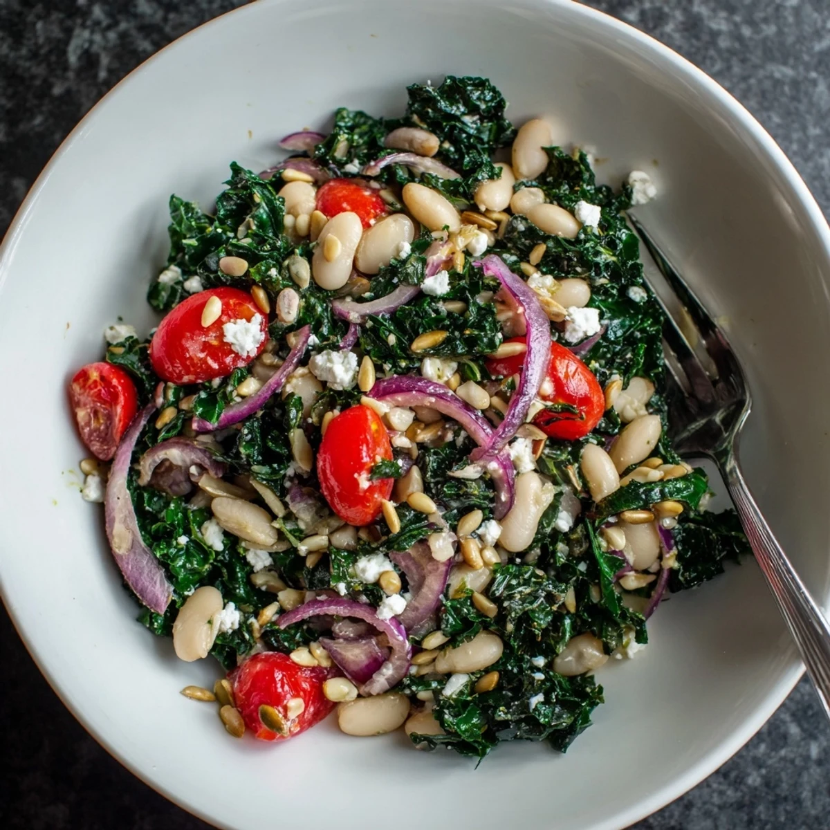 A close-up of a bowl of White Bean and Kale Salad, showcasing cherry tomatoes and thinly sliced red onion on a rustic wooden table.