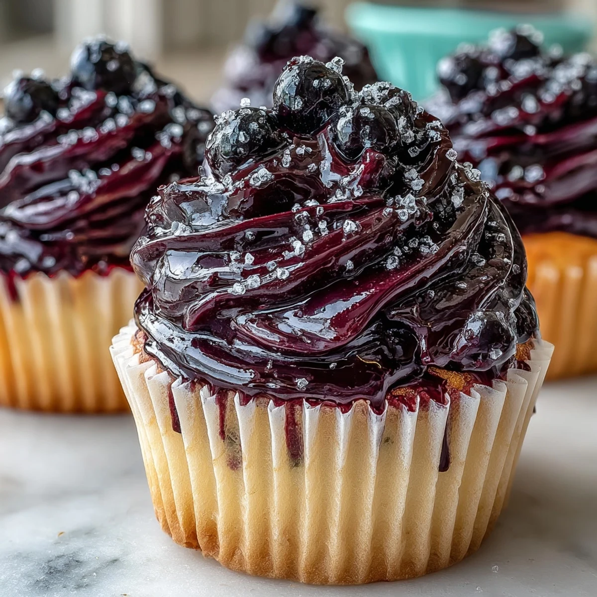Black Currant Frosting piped onto petit fours garnished with fresh berries near a whisk and bowl.