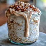Close-up of creamy High-Protein Cinnamon Roll Overnight Oats in a glass jar, topped with a luscious cream cheese drizzle and a dusting of cinnamon.