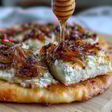 A close-up of Goat Cheese & Caramelized Onion Flatbread with bubbling cheese and caramelized onions.