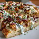 Close-up of a bubbly Lemon Feta Chicken Naan Pizza with melted mozzarella, Kalamata olives, and a creamy tzatziki drizzle.