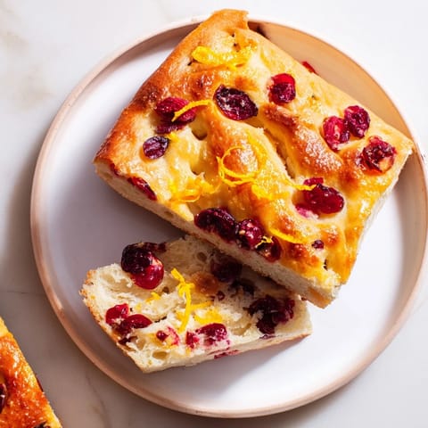 A close-up of a bubbling Cranberry Orange No-Knead Focaccia, showing the soft, airy texture and golden crust.