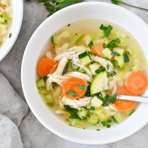 Colorful Spring Garden Chicken Soup with vibrant green peas, diced zucchini, and shredded chicken swimming in a golden, herb-infused broth.  