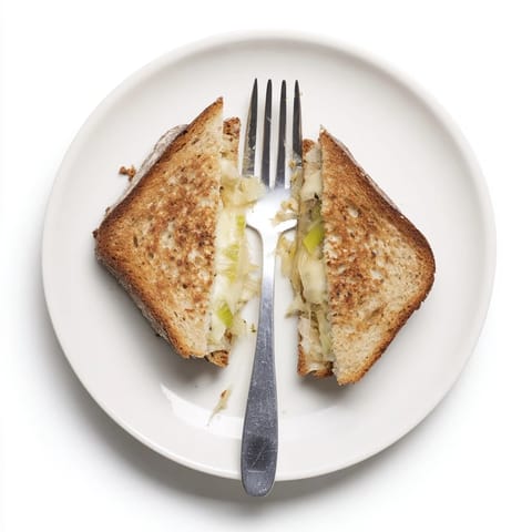 A warm Havarti & Caramelized Leek Grilled Cheese halves to reveal gooey cheese and tender leeks beside a fresh green salad.  