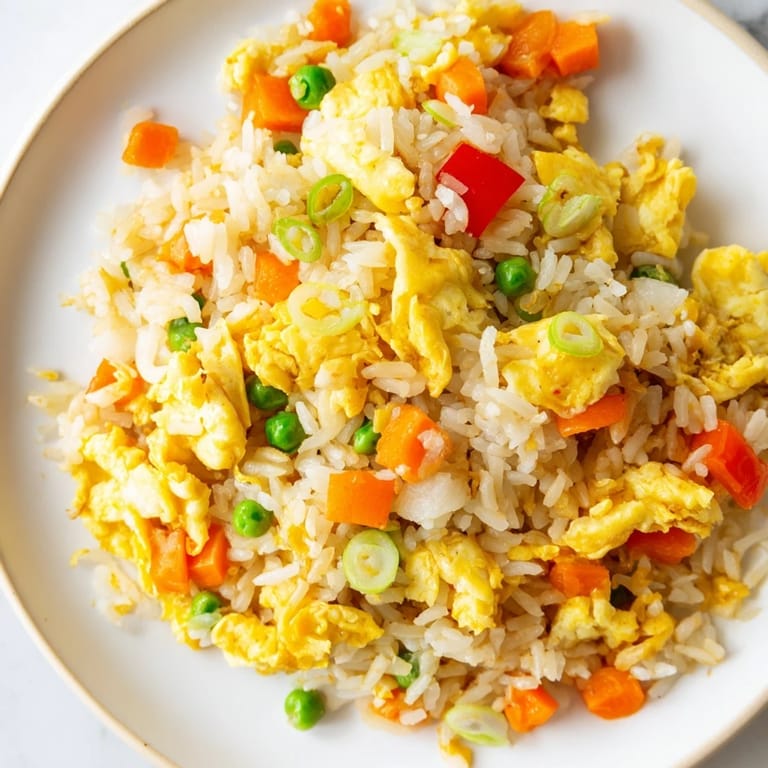 A close-up of classic Egg Fried Rice with glistening soy sauce, scallions, and tender vegetables ready to eat.  