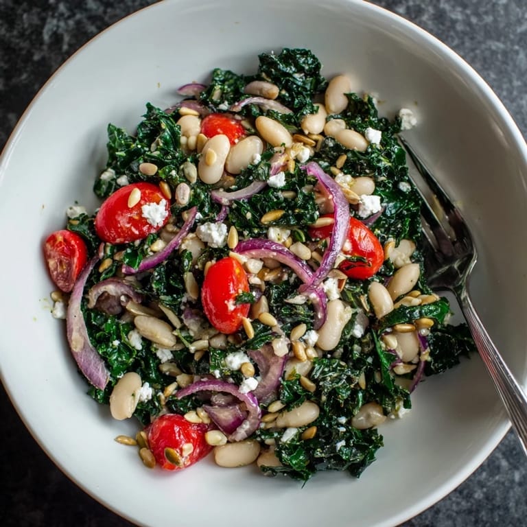 A close-up of a bowl of White Bean and Kale Salad, showcasing cherry tomatoes and thinly sliced red onion on a rustic wooden table.